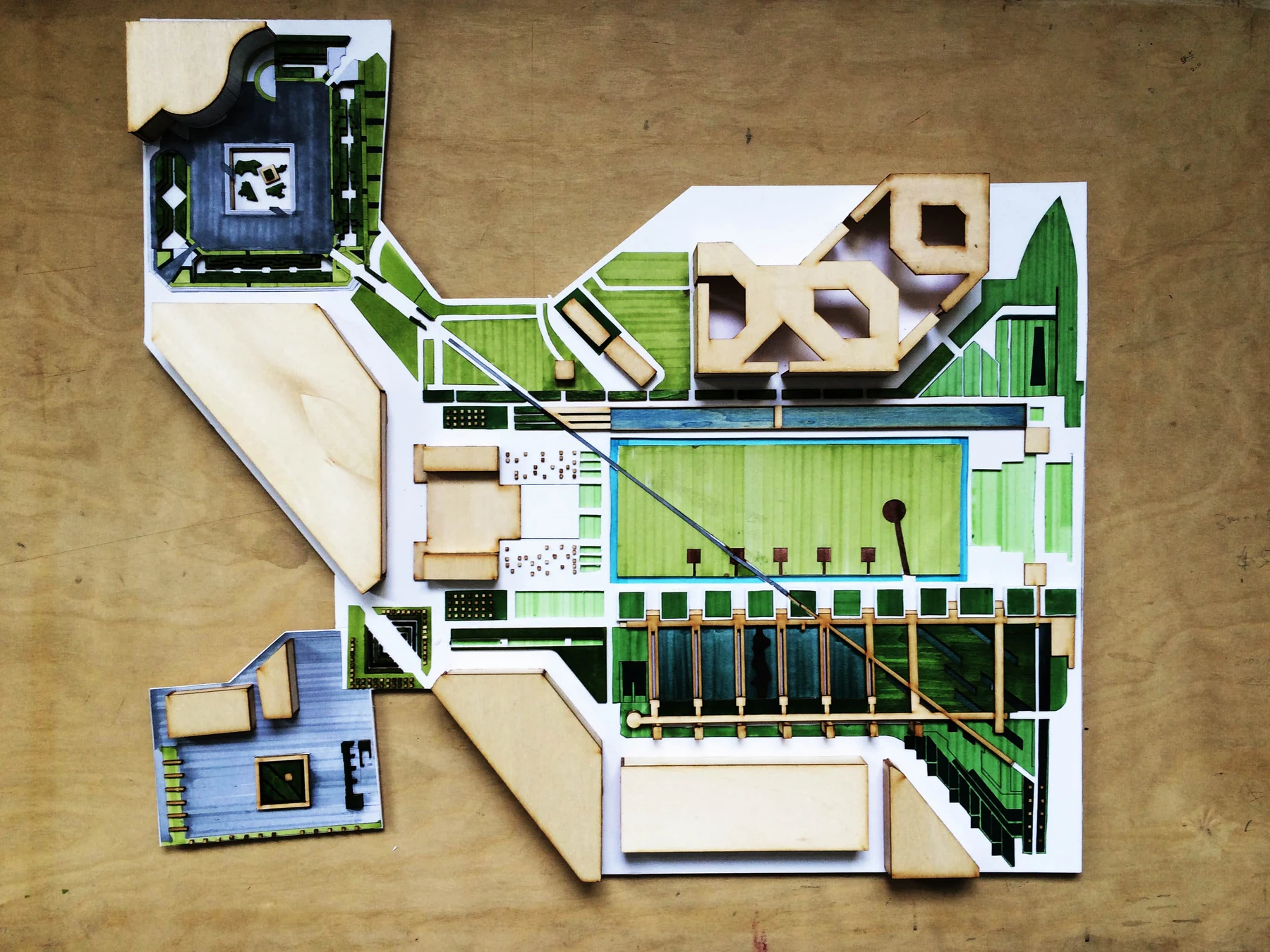 Overhead photograph of an architectural ensemble model with green landscape strips, paths and a central water feature